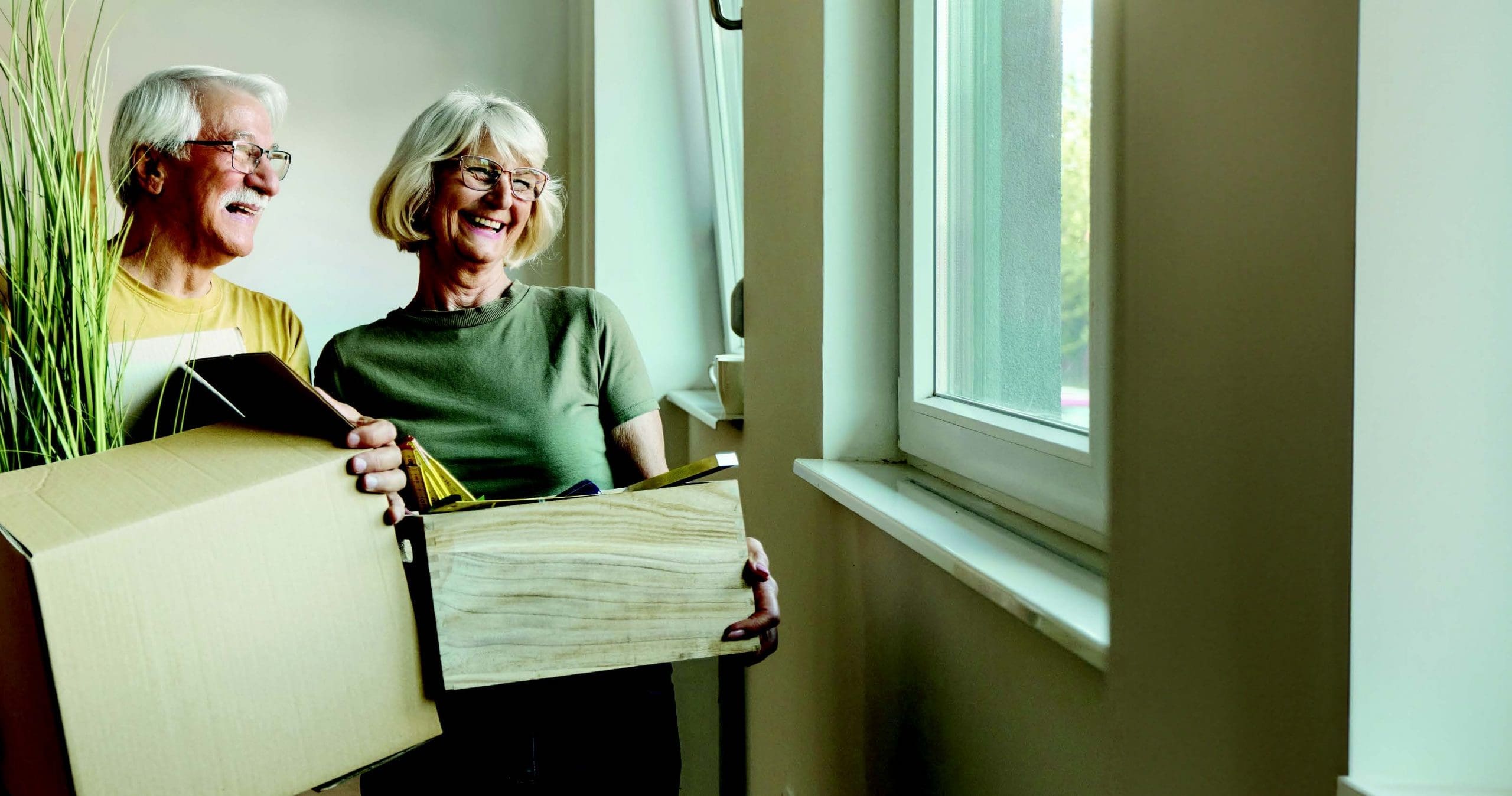 senior couple smiling and carrying moving boxes