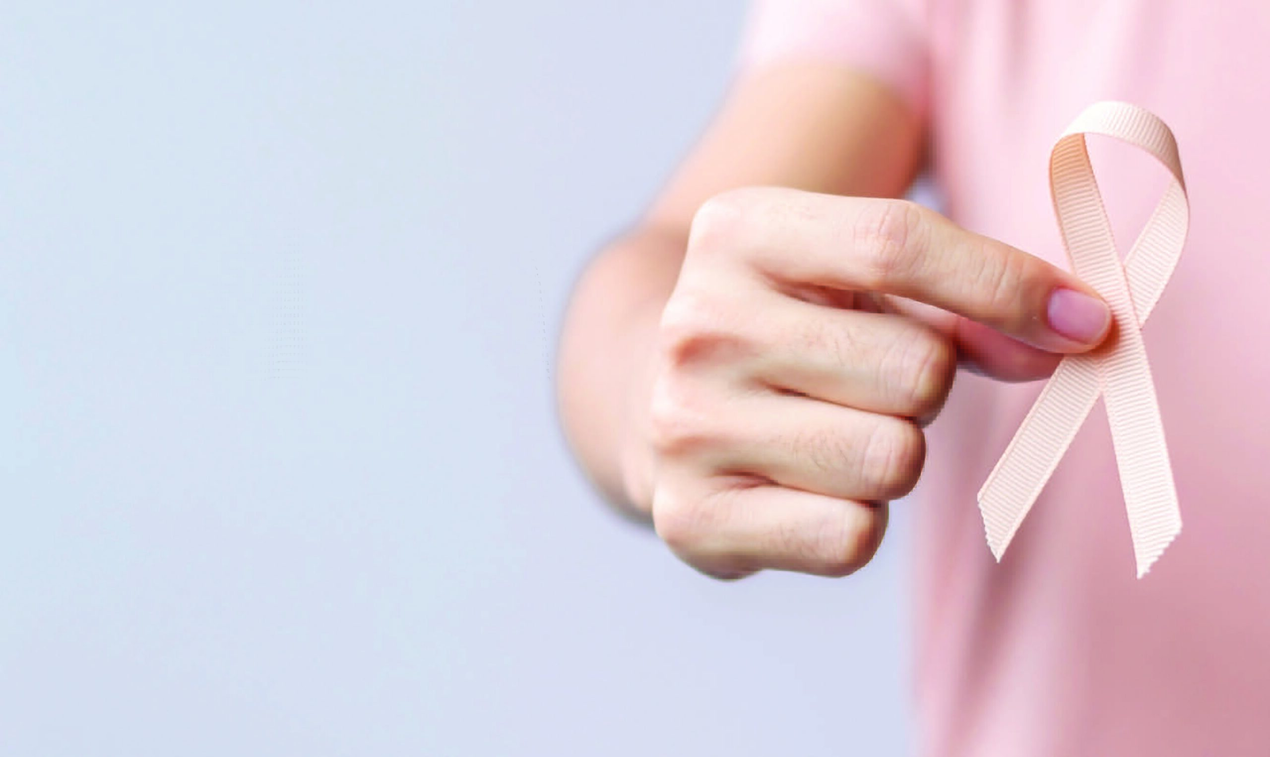 close up of a person holding up a pink, cancer awareness ribbon