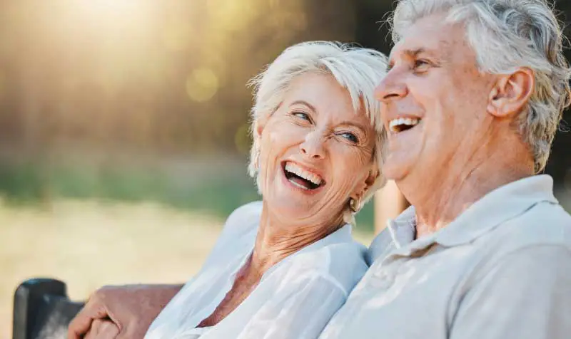a senior couple laughing together while sitting outside on a park bench