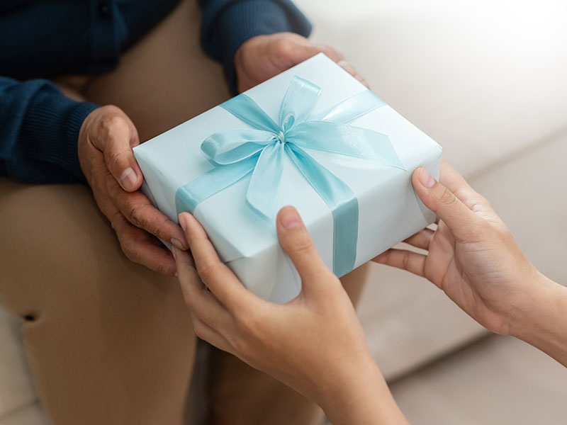 close-up of a person giving another person a gift with light blue wrapping paper and a dark blue bow.