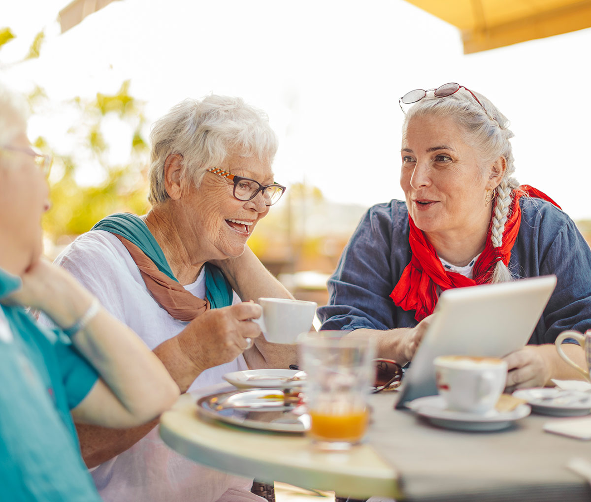 senior women drinking coffee and smiling while looking at a tablet device